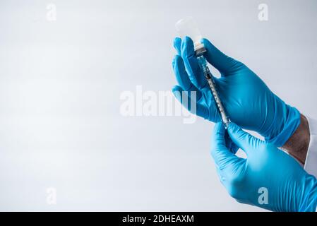 Mani in guanti che aspirano il vaccino nella siringa su sfondo bianco. Foto Stock