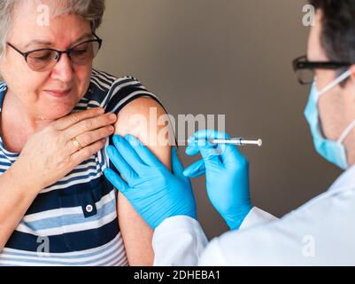 Donna anziana che viene iniettata con un vaccino dal medico nella parte superiore del braccio. Foto Stock
