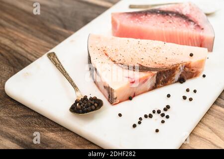 Pesce spada crudo. Due pezzi di bistecche di pesce fresco crudo con sale e pepe nero da vicino sul tagliere di marmo su sfondo di legno Foto Stock