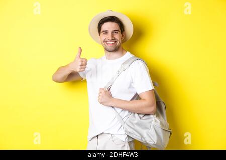 Concetto di turismo, viaggio e vacanza. Uomo felice che va in vacanza, tenendo lo zaino e mostrando il pollice in su, sorridente soddisfatto, Foto Stock
