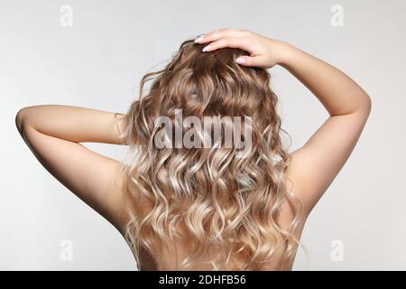 Donna dal retro su sfondo grigio. Femmina con capelli ricci Foto Stock