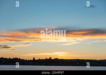 Quando il sole tramonta, la focalizzazione è su una nuvola lenticolare diventa arancione luminoso nel cielo blu chiaro sopra la silhouette in primo piano e sopra il lago Tekapo Nuova Zelanda. Foto Stock