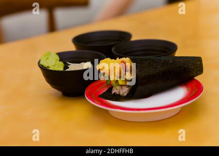 Gamberetti tempura, cetrioli, riso e germogli di daikon avvolti in alghe, con ciotola di wasabi e zenzero sul tavolo Foto Stock
