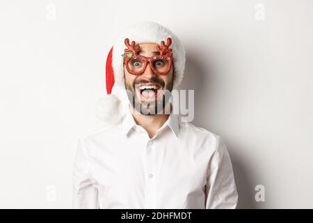 Primo piano di un uomo eccitato bearded in occhiali di natale e cappello di santa guardando stupito offerta promozionale, pubblicità vacanze invernali Foto Stock
