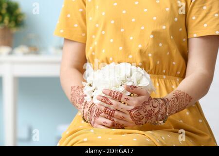 Bella donna con tatuaggio henné sulle mani e fiori a casa Foto Stock