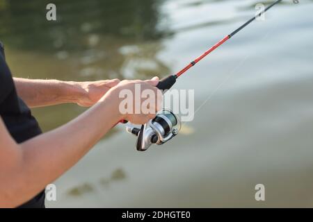 Le mani del pescatore stanno pescando su una filatura nell'acqua in una giornata estiva soleggiata. Foto Stock