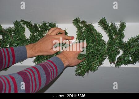 Le mani dell'uomo che decorano il muro con il ramo di Natale Foto Stock