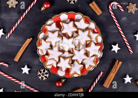 Biscotti di Natale alla cannella smaltati a forma di stella tedeschi chiamati 'Zimtsterne' ON piatto a righe circondato da bastoncini di cinnammon e decorazioni stagionali Foto Stock