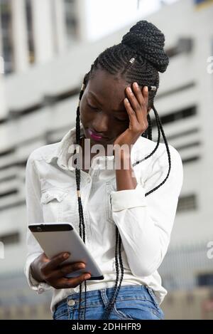 Attraente donna di affari stanca in abiti formali usando un intelligente telefono che soffre mal di testa in città Foto Stock