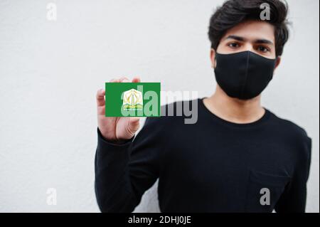 Uomo indonesiano indossare tutto nero con maschera faccia tenere in mano la bandiera Aceh isolato su sfondo bianco. Province dell'Indonesia coronavirus concetto. Foto Stock