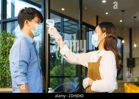 Donna asiatica dipendente caffè dopo prendere temperatura asiatico con l'uomo maschera prima di andare al ristorante o caffè per nuovo coronavirus stile di vita normale Foto Stock