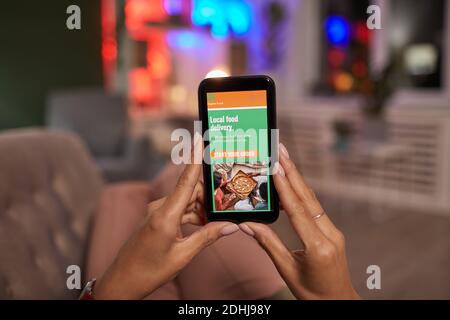 Primo piano di una donna che tiene il telefono cellulare e ordinare cibo online mentre si sdraiano sul divano Foto Stock