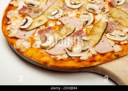 Deliziosa pizza a base di carne servita su un piatto di legno, ingredienti salsa Signature, mozzarella, prosciutto, pancetta, cetriolo sottaceto, funghi su bianco. Pizzica Foto Stock