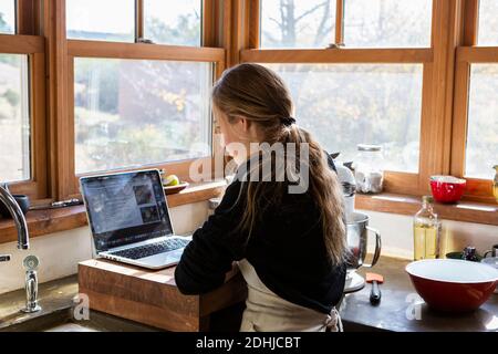 Ragazza adolescente in cucina seguendo una ricetta di cottura su un computer portatile. Foto Stock