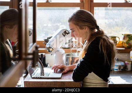 Ragazza adolescente in cucina seguendo una ricetta di cottura su un computer portatile. Foto Stock