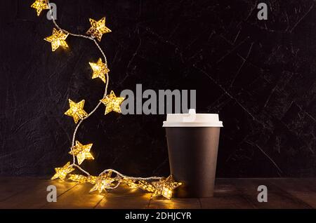 Tazza da caffè di carta bianca nera grande da portare via con luci dorate di natale illuminanti con stelle in interni scuri, mock up per la pubblicità, caffè, bar, r Foto Stock