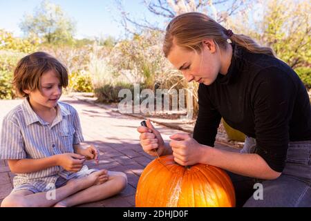 La ragazza adolescente e il suo fratello più giovane intagliano le zucche sul patio. Foto Stock