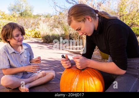 La ragazza adolescente e il suo fratello più giovane intagliano le zucche sul patio. Foto Stock