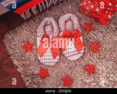 Sfondo natalizio di morbide pantofole bianche per la casa e decorazioni natalizie rosse con scatole regalo. Disposizione piatta, vista dall'alto. Idee regalo di nuovi anni. Foto Stock