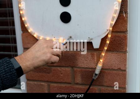 Primo piano di mans Hand che mette in su le luci domestiche di Natale per la stagione di festa. Avvitamento della luce per pupazzo di neve per alloggiare la parete all'esterno in inverno Foto Stock