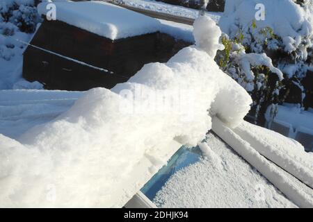 primo piano di neve coperto tetto serra, attraverso finestra. tetti e alberi con neve profonda deriva fuori in inverno Foto Stock