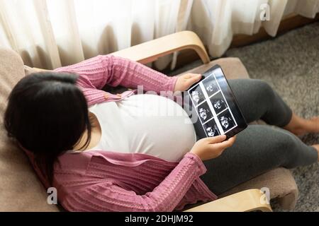 Donna incinta che si sente felice a casa mentre si prende cura del suo bambino. La giovane madre in attesa di tenere il bambino in pancia incinta. Maternità prenatale Foto Stock