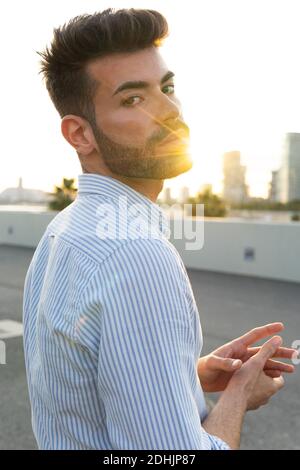 Vista posteriore di un bel maschio determinato in un abito elegante strada della città guardando la macchina fotografica sullo sfondo del tramonto Foto Stock