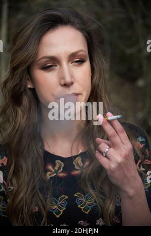 Donna che fuma la sigaretta e che esala il fumo mentre si è in piedi natura e guardare lontano Foto Stock