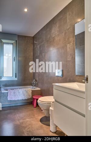 Interno del bagno in colori bianco e beige con vasca e servizi igienici in appartamento contemporaneo Foto Stock