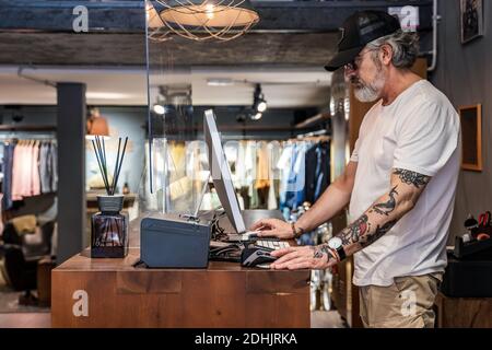 Vista laterale del proprietario del negozio di abbigliamento che controlla le vendite sul computer Foto Stock