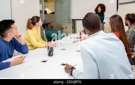 Colleghi multirazziali concentrati seduti intorno al tavolo ascoltando la voce femminile durante la presentazione e la discussione della strategia aziendale nel lavoro moderno Foto Stock