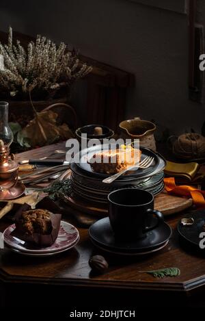 Viene servito un pezzo di deliziosa torta di zucca e muffin al cioccolato su tavolo di legno con set da tè in camera buia Foto Stock