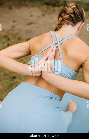 Vista posteriore di femmina sottile in abbigliamento sportivo facendo mezza piramide Posa con le mani di preghiera dietro la schiena mentre si pratica yoga in natura Foto Stock