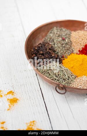 Alto angolo di ciotola di legno riempito con vari tipi di colorate spezie aromatiche secche su tavolo di legno bianco Foto Stock