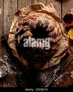 Dall'alto fresco gustoso Kugelhopf sul tavolo di legno stagionato vicino foglie di autunno asciutte Foto Stock