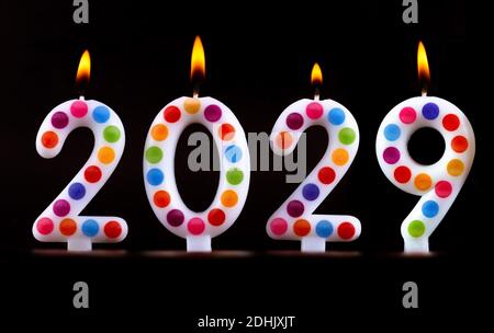 Quattro candele colorate scrivono numeri fiamma felice anno nuovo 2029 sfondo nero Foto Stock
