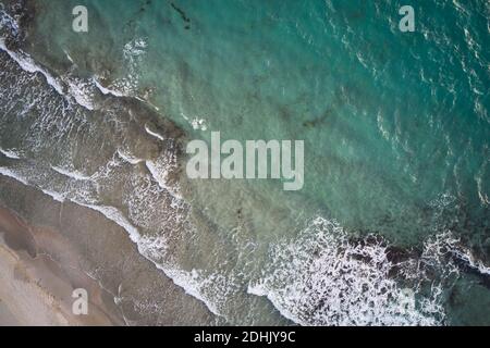 Vista aerea dall'alto dell'acqua turchese con alghe e schiuma onde che rotola su una spiaggia di sabbia vuota Foto Stock