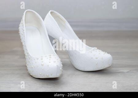 Le scarpe da sposa bianche con perle sono sul pavimento. Gli accessori della sposa Foto Stock