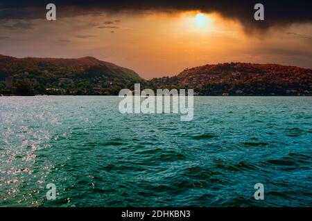 Lago di Como bello drammatico cielo arancione tramonto sulle montagne paesaggio turchese orizzonte d'acqua con città e villaggi sull'altra riva della Lombardia, esso Foto Stock