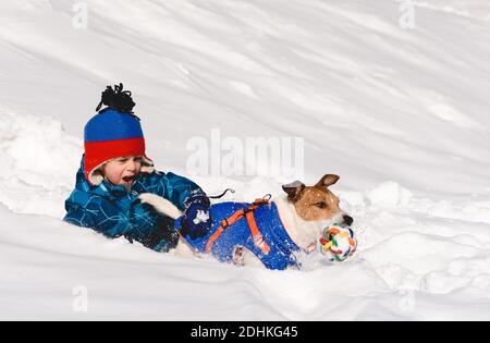Ragazzo con espressione emotiva del volto che gioca con il cane da compagnia di famiglia nella neve durante il giorno d'inverno Foto Stock