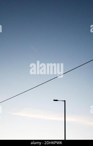 Un'immagine semplice di un'unica lampada da strada e di un tetto linea di alimentazione Foto Stock