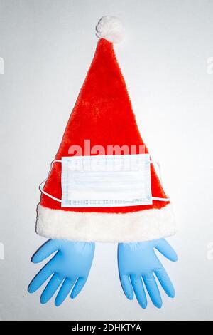 Cappello di Natale rosso e bianco con maschera chirurgica e un paio di guanti in vinile blu gonfiati. Vista dall'alto verticale Foto Stock