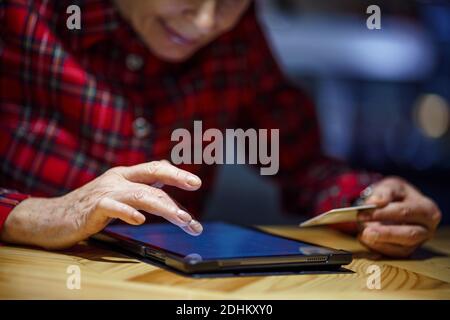 Donna anziana che ordina regali di Natale online su tablet digitale in caffetteria. Acquirente maturo che detiene il PC tablet e la carta di credito. Donna anziana shopping Foto Stock