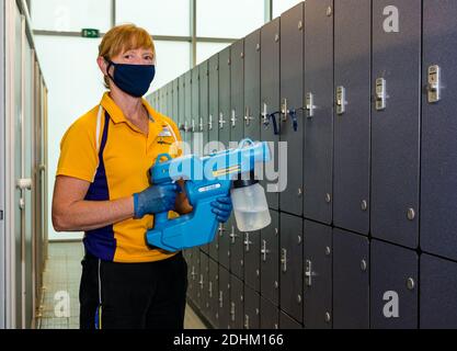 Membro femminile del personale che indossa armadietti per la pulizia della maschera facciale con spruzzatore per l'igiene Fimap, North Berwick sEnjoy Leisure Ports Center, Scozia, Regno Unito Foto Stock