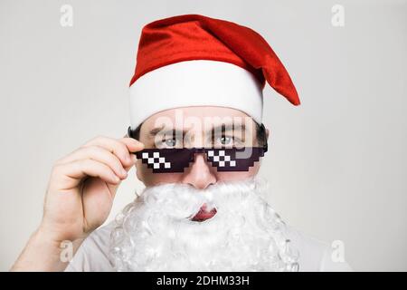 Babbo Natale in divertenti occhiali da sole pixelati su sfondo bianco. Gangster, boss, meme di vita del delinquere. stile a 8 bit. Holly Jolly x Mas Noel. Freddo Foto Stock