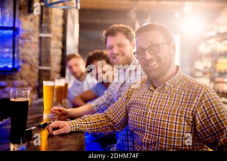 Fila di uomini seduti al bar con birra alla spina chiara e scura e guardando la macchina fotografica. Foto Stock