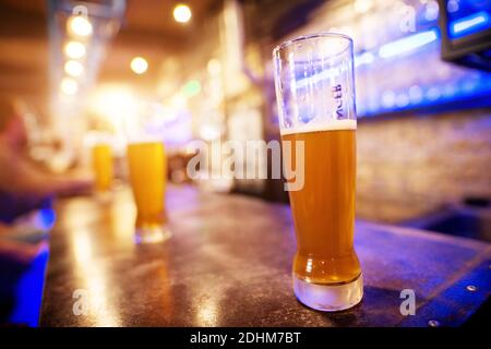 Vista ravvicinata del bicchiere di birra alla spina collocato su un tavolo da bar con una fila di altri sullo sfondo. Foto Stock