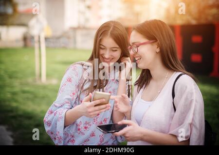 Due belle ragazze sorridenti della scuola superiore che mostrano messaggi l'un l'altro da un cellulare mentre si levano in piedi fuori nel parco. Foto Stock