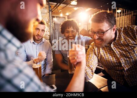 Primo piano di giocosi uomini multiculturali che si divertono nel pub. Due amici lottano con le braccia mentre altri sostengono. Foto Stock