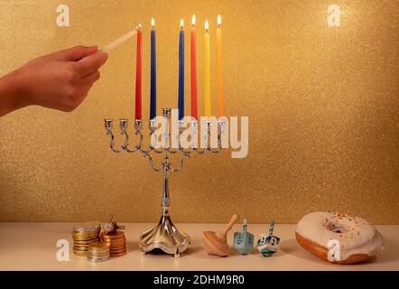 Giorno 6 della festa religiosa ebraica Hanukkah con la mano del bambino illuminazione 6 ° candela in menorah tradizionale lampadario su luccicanti dorati sfondo wit Foto Stock